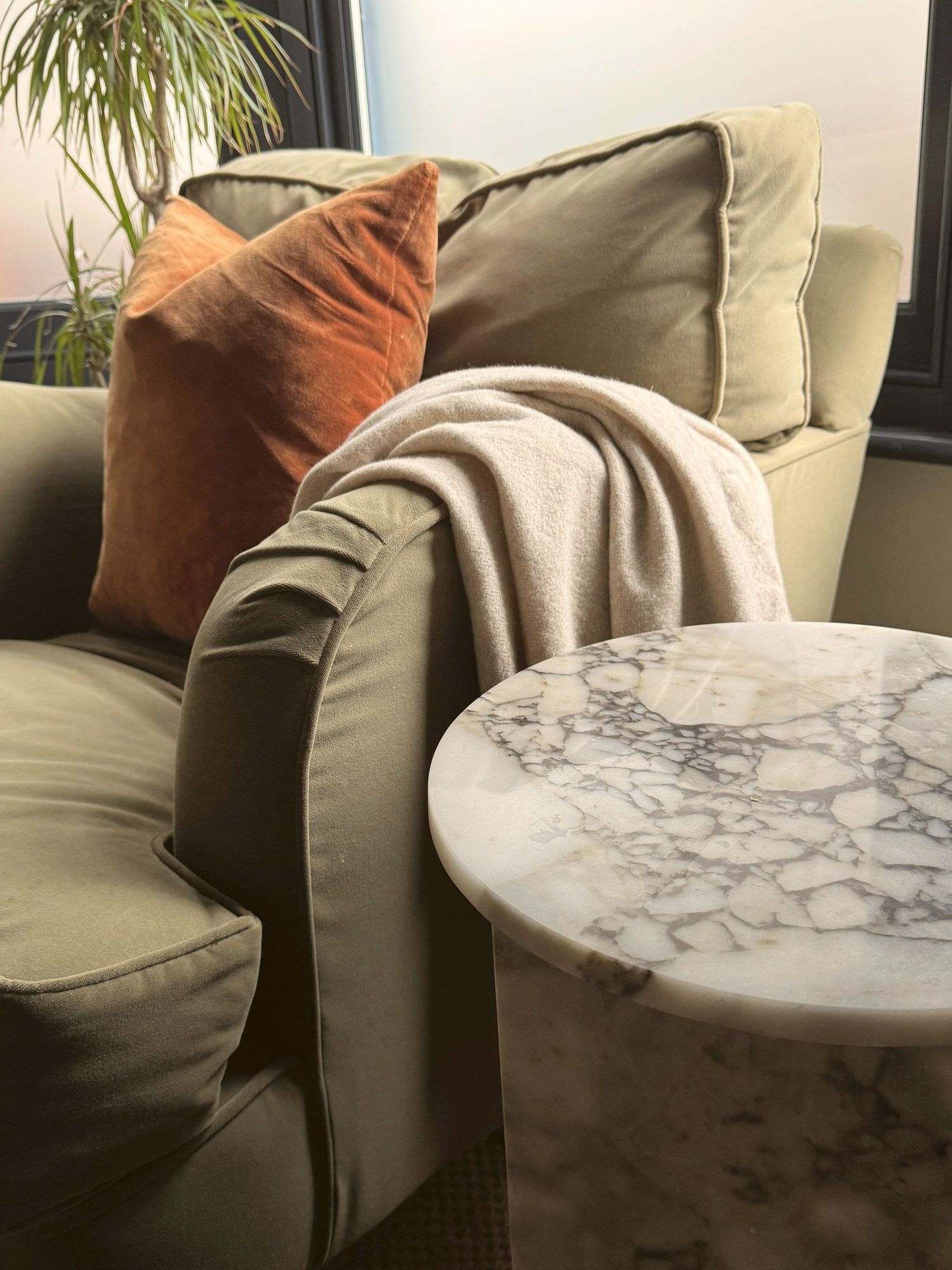 Olive velvet sofa with rust cushion and marble side table
