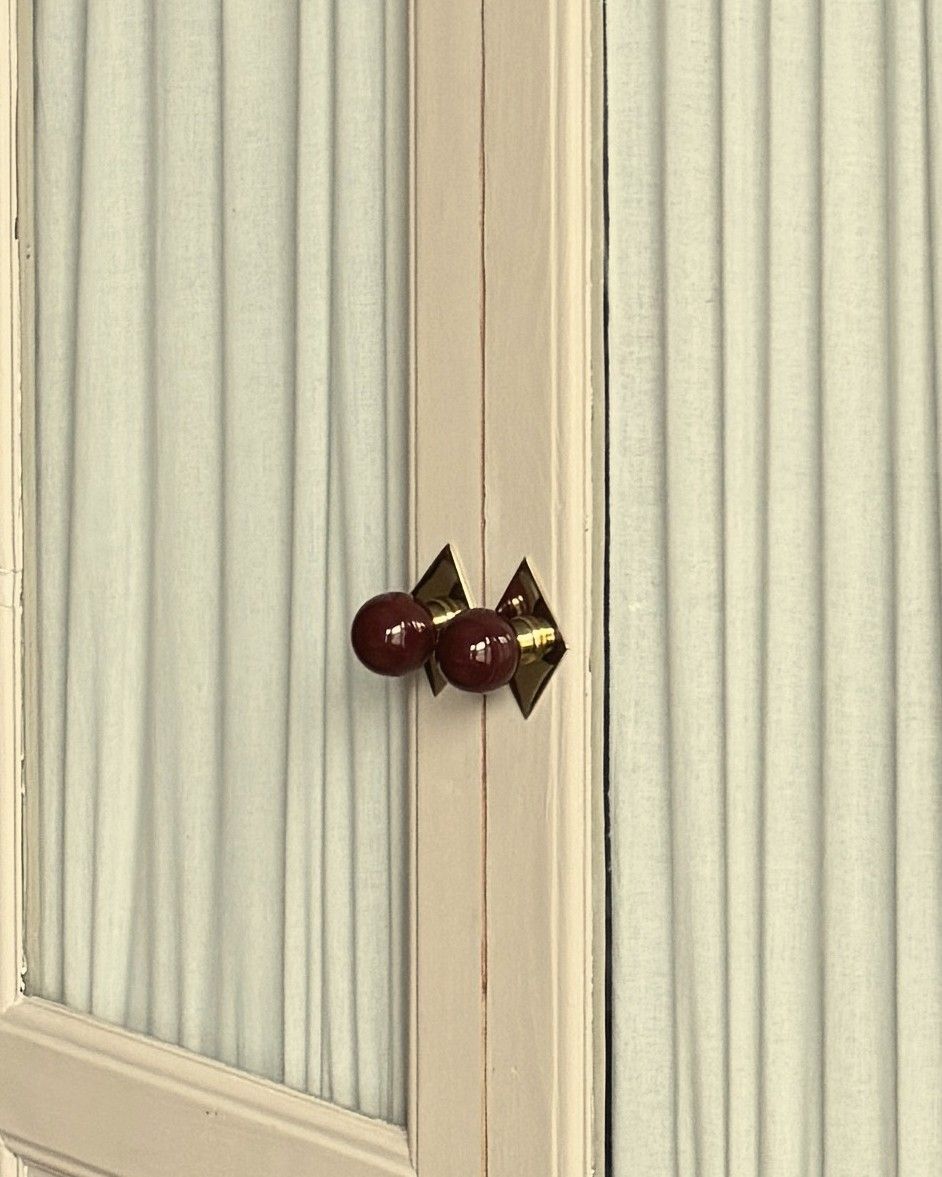 Painted wardrobe doors with gathered linen behind the glass and burgundy knobs on brass diamond backplates